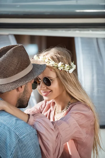 Hippie casal em óculos de sol abraçando e olhando um para o outro perto reboque — Fotografia de Stock