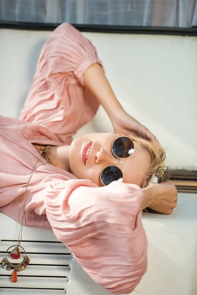 Attractive hippie girl in sunglasses lying on camper van — Stock Photo