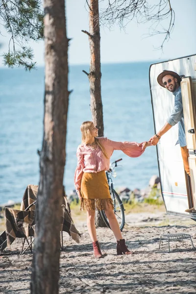 Пара хиппи держась за руки и отправляясь на прогулку в кемперван возле моря — стоковое фото