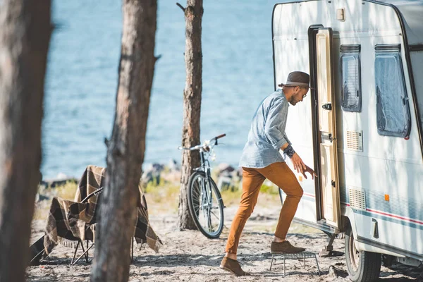 Young man going into trailer in camp with bicycle near the sea — Stock Photo