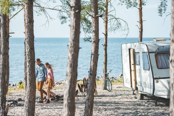 Joven pareja cogida de la mano y caminando en la naturaleza cerca de campervan - foto de stock