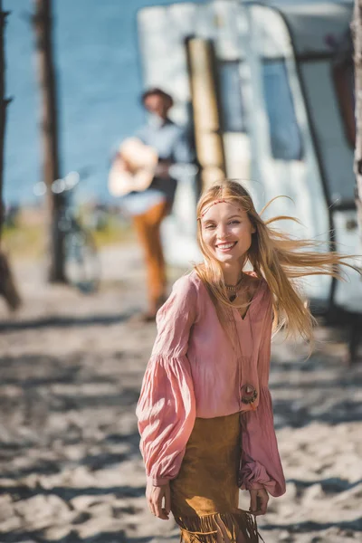 Усміхнена дівчина хіпі танцює, поки чоловік грає на гітарі біля кампервана — стокове фото