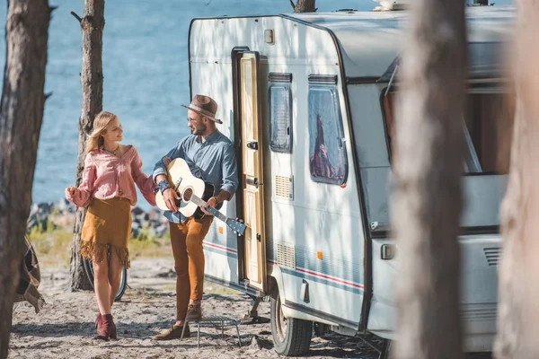 Hippie copine danse tandis que copain jouer de la guitare près de remorque dans la nature — Photo de stock