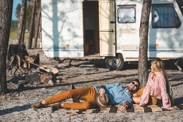 Young happy couple relaxing on blanket near camper van — Stock Photo