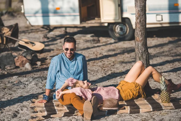 Hippie casal relaxante em cobertor perto de reboque na natureza — Fotografia de Stock