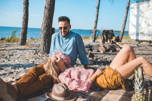 Belo casal hippie descansando sobre cobertor perto de reboque na natureza — Fotografia de Stock