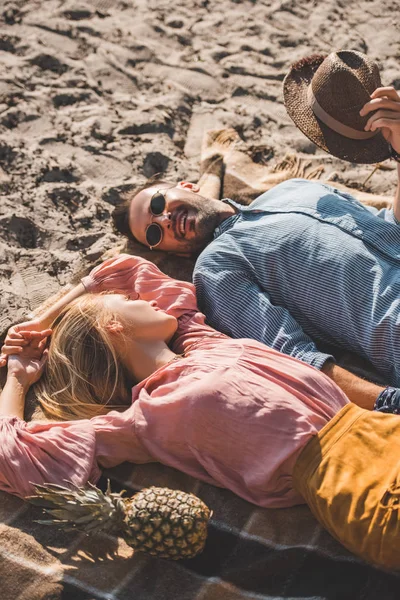 Hippie couple looking at each other and relaxing on blanket on sand — Stock Photo