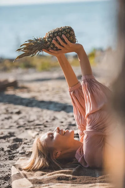 Attraktives, glückliches Mädchen, das auf einer Decke liegt und frische Ananas hält — Stockfoto