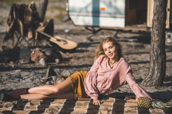 Beautiful hippie girl resting on blanket with pineapple near camper van — Stock Photo