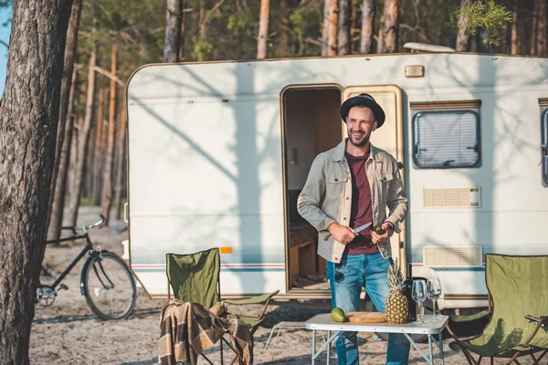 Uomo sorridente taglio avocado vicino camper nella foresta — Foto stock