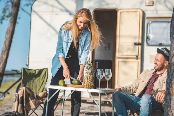 Attractive woman cutting avocados while handsome man sitting near in camp — Stock Photo