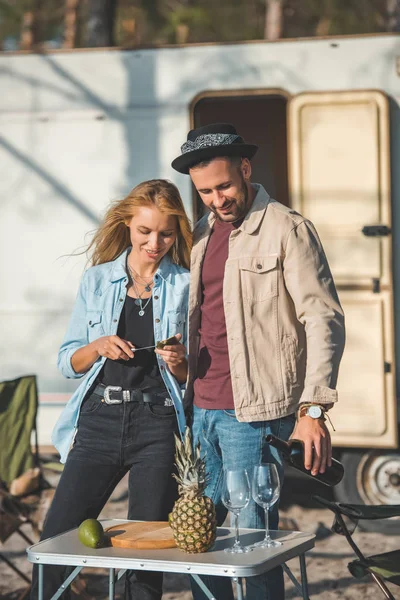 Young happy couple having picnic with wine, pineapple and avocado near campervan — Stock Photo