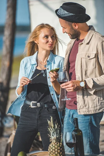Schöne Mädchen schneidet Avocado, während sie ihren Freund mit einem Glas Wein anschaut — Stockfoto