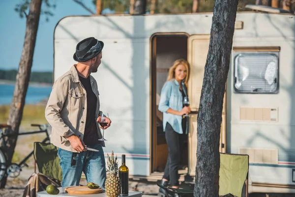 Selective focus of handsome man with glass of wine looking at girlfriend near trailer — Stock Photo