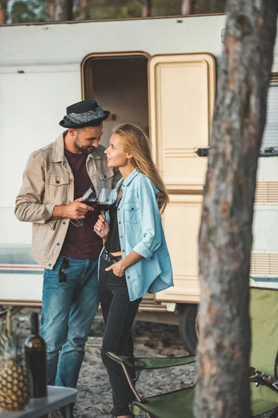 Young happy couple clinking with glasses of wine and looking at each other near trailer — Stock Photo
