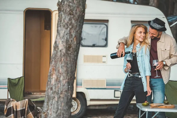 Young man pouring red wine for attractive girlfriend near campervan — Stock Photo