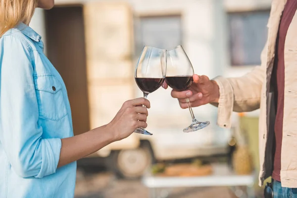 Vista recortada de pareja tintineo con copas de vino tinto cerca campervan - foto de stock