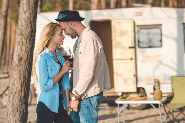 Hermosa pareja feliz tocando la frente y sosteniendo copas de vino cerca campervan - foto de stock