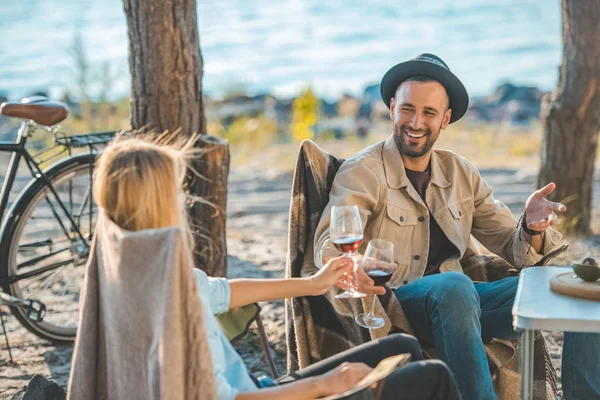 Hermosa pareja con copas de vino hablando durante un picnic cerca del mar - foto de stock