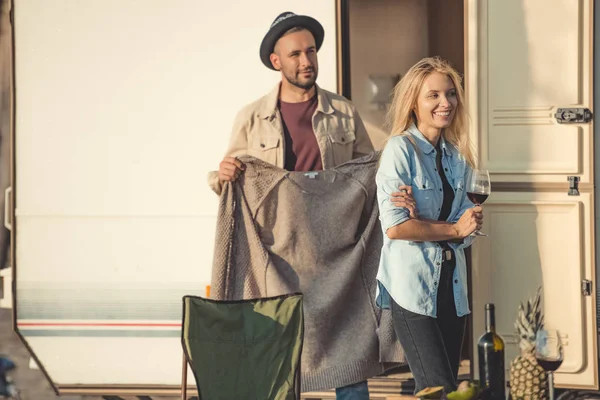 Handsome man wearing warm sweater on his girlfriend near trailer — Stock Photo