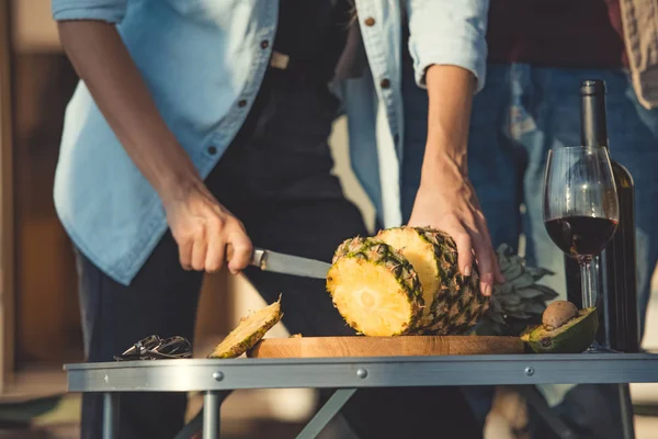 Partial view of woman cutting pineapple on wooden board with wine near — Stock Photo