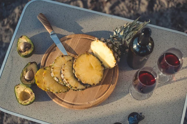 Top view of pineapple on cutting board with avocados and bottle of red wine near on table — Stock Photo