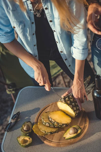Cropped view of girl cutting pineapple on wooden board — Stock Photo