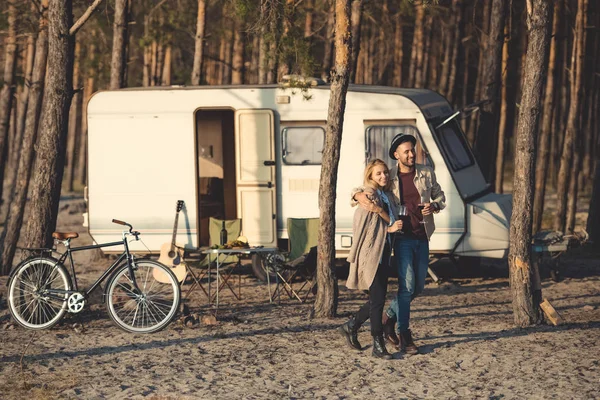 Homme étreignant petite amie avec du vin et marchant près de camping-car — Photo de stock