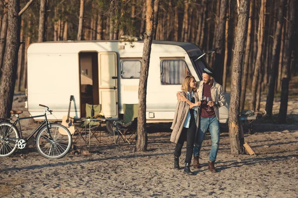 Joven feliz pareja con copas de vino caminando cerca campervan - foto de stock