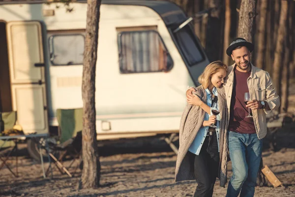 Schönes Paar mit Weingläsern, die sich umarmen und in der Nähe von Wohnmobil spazieren gehen — Stockfoto