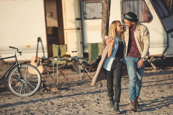 Sonriente pareja abrazándose, mirándose y caminando cerca de campervan - foto de stock