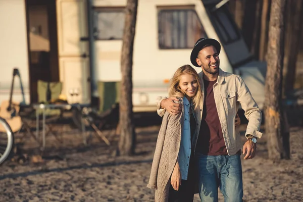 Smiling man hugging woman near trailer in forest camp — Stock Photo