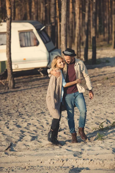 Glückliches junges Paar umarmt und spaziert in der Nähe von Wohnwagen im Wald — Stockfoto