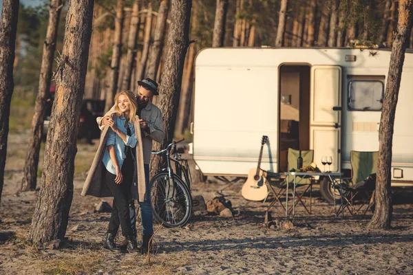 Joven feliz pareja abrazando en el campamento con remolque, bicicleta y guitarra - foto de stock