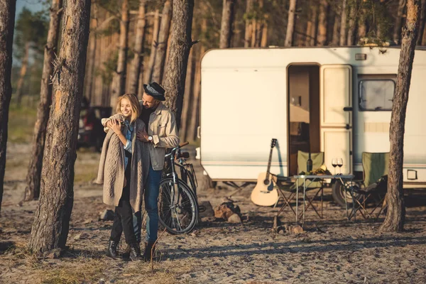 Happy couple of lovers embracing in forest camp with trailer, bicycle and guitar — Stock Photo