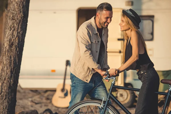 Hermosa pareja sonriente de pie junto con la bicicleta cerca de autocaravana - foto de stock