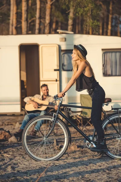 Selective focus of beautiful woman with bicycle and man playing guitar near campervan — Stock Photo