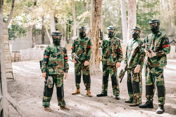 Paintball team in uniform and goggle masks standing with paintball guns outdoors — Stock Photo