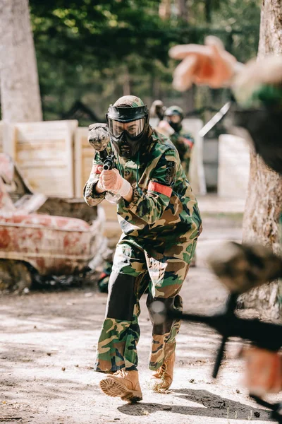 Vista parcial del jugador de paintball en uniforme haciendo sígueme gesto a su equipo al aire libre - foto de stock