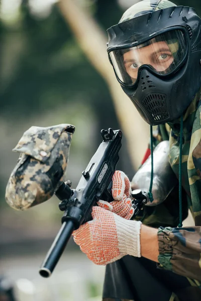 Male paintball player in goggle mask and camouflage with paintball gun outdoors — Stock Photo