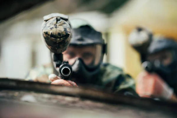 Selective focus of paintball team in uniform and protective masks aiming by paintball guns outdoors — Stock Photo