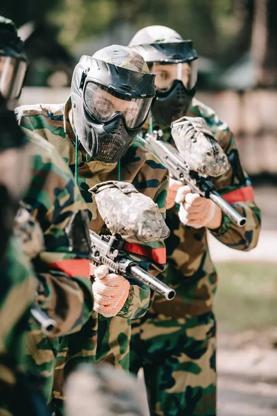 Joueurs de paintball masqués et uniformes de camouflage tenant les pistolets de paintball à l'extérieur — Photo de stock
