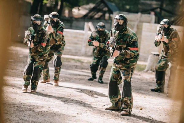 Paintball team in uniform and protective masks playing paintball with marker guns outdoors — Stock Photo