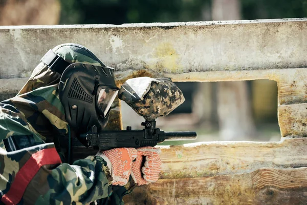 Visão traseira do jogador de paintball em máscara de óculos e camuflagem visando por pistola de paintball ao ar livre — Fotografia de Stock