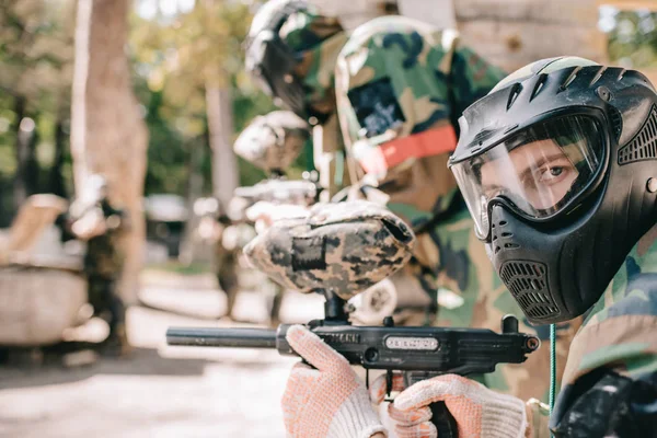 Porträt eines männlichen Paintballspielers in Schutzmaske, der eine Marker-Pistole in der Hand hält und in die Kamera schaut — Stockfoto