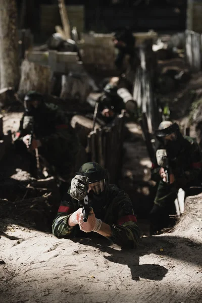 Paintball team in camouflage and protective masks aiming by marker guns from ditch outdoors — Stock Photo