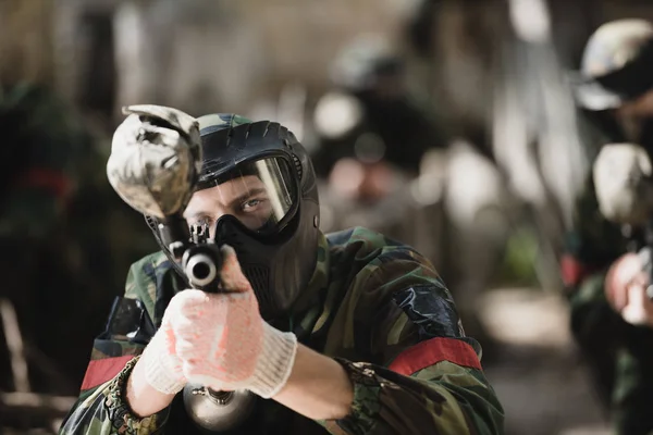 Selective focus of serious male paintball player in goggle mask and camouflage aiming by paintball gun outdoors — Stock Photo