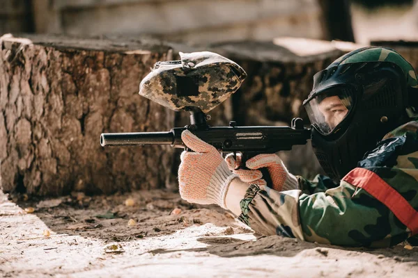 Jugador de paintball masculino enfocado en máscara de gafas y camuflaje con el objetivo de pistola de paintball al aire libre - foto de stock