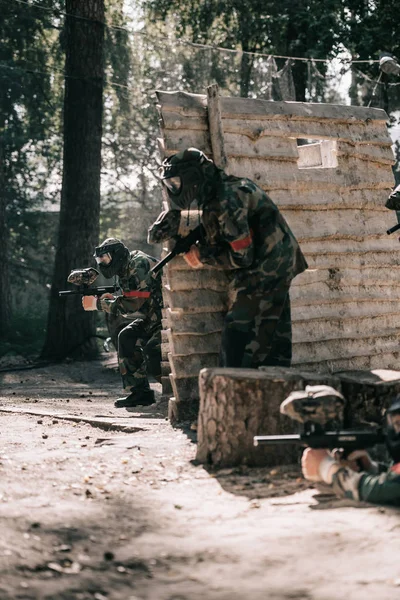 Paintball team in uniform and protective masks playing paintball with marker guns outdoors — Stock Photo