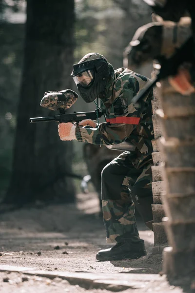 Enfoque selectivo del jugador de paintball masculino en máscara de gafas y camuflaje con el objetivo de pistola de paintball al aire libre - foto de stock